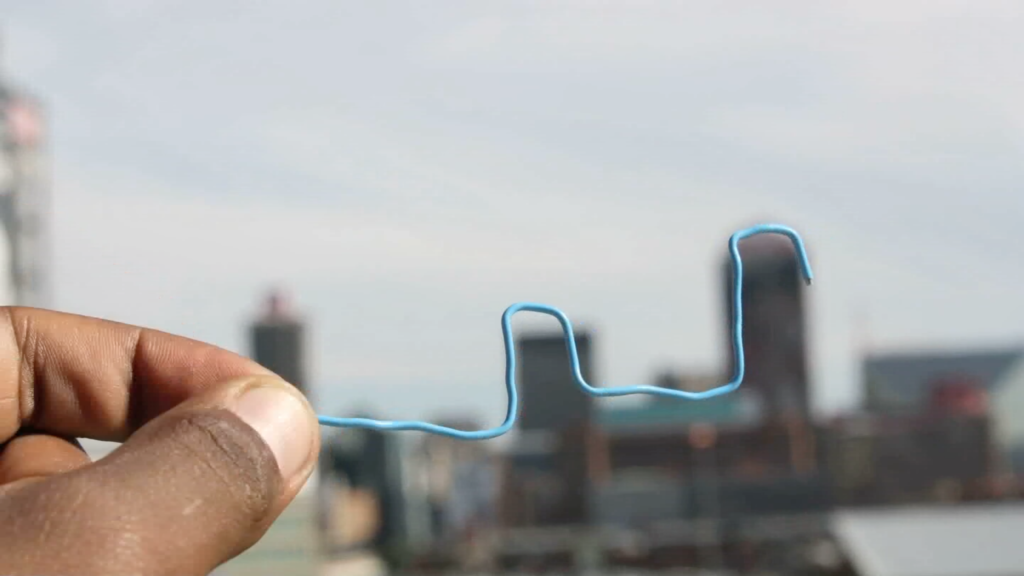 Two hands hold a stretched out paper clip that trace the outline of buildings along a skyline.