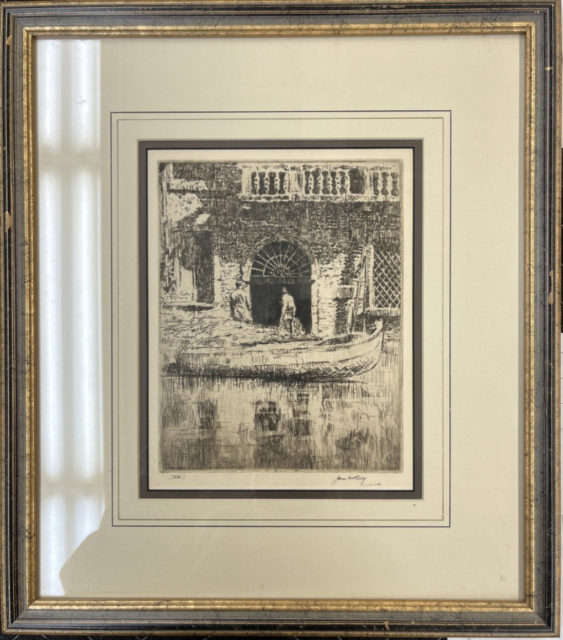 A framed artwork. It is an etching of a scene in Venice, Italy. There is a boat coming from the left side, and a doorway, as well as two figures, in the center. There is a reflection on the water.