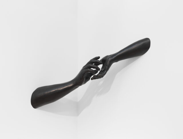 Bronze sculpture of two black bronze arms protruding from the wall, reaching towards each other
