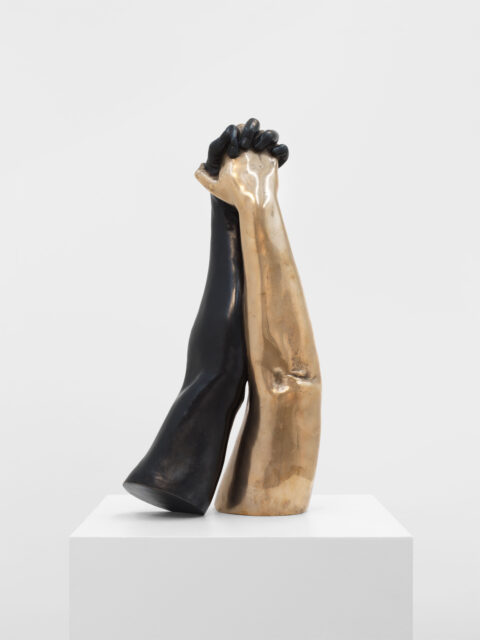 One black bronze arm and one gold bronze arm holding hands on top a pedestal